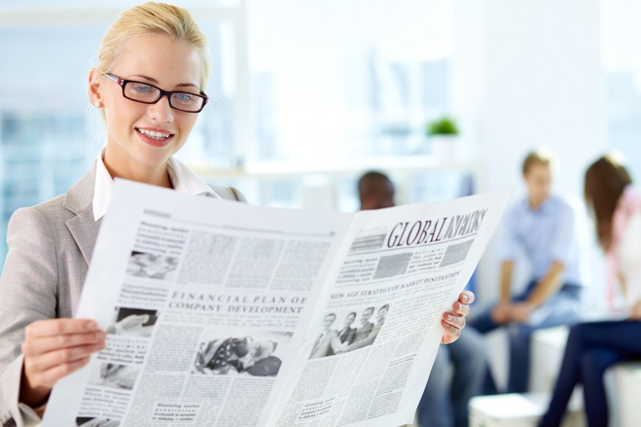 Portrait of happy female reading newspaper in working environment